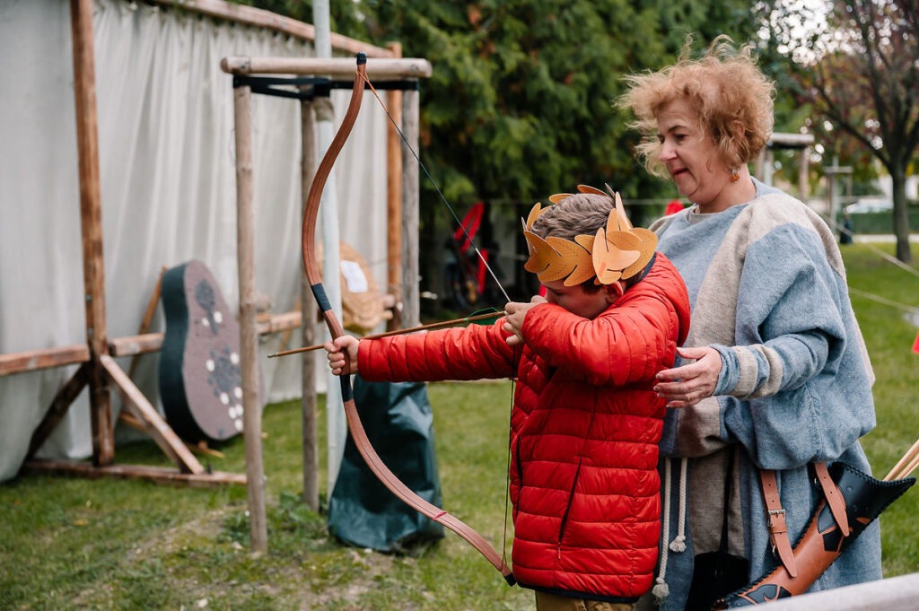 Rímske hry 2025, dieťa s rímskou korunou skúša lukostreľbu