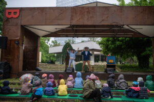Kultúrna scéna v Sade Janka Kráľa, BMD 2025, deti sedia na lavičkách a sledujú vystúpenie