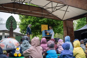 Kultúrna scéna v Sade Janka Kráľa, BMD 2025, deti v pršiplášťoch sedia na lavičkách a sledujú vystúpenie