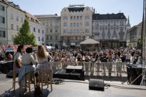 Hlavné námestie, na pódiu vystupuje Paper Moon Trio, námestie je plné posluchádov a poslucháčiek