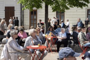 Návštevníci a návštevníčky BMD 2025 sedia na červených setoch Sadni si! a sledujú kultúrny program