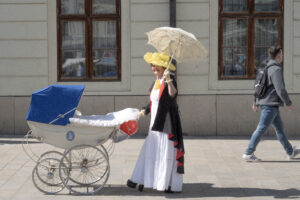 Dáma v dobovom oblečení so slnečníkom tlačí dobový kočík