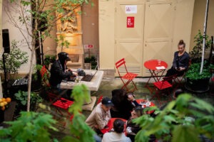 Raylab DJ Set na Bielej počas BMD 2025, návštevníci*čky sedia na červených stoličkách na nádvorí