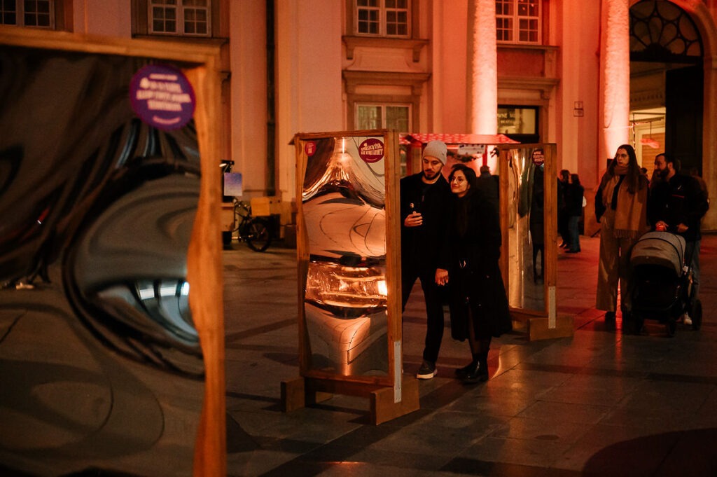 Inštalácia krivých zrkadiel na Festivale mladého vína 2025, muž a žena stoja pri zrkadle a sledujú svoj odraz