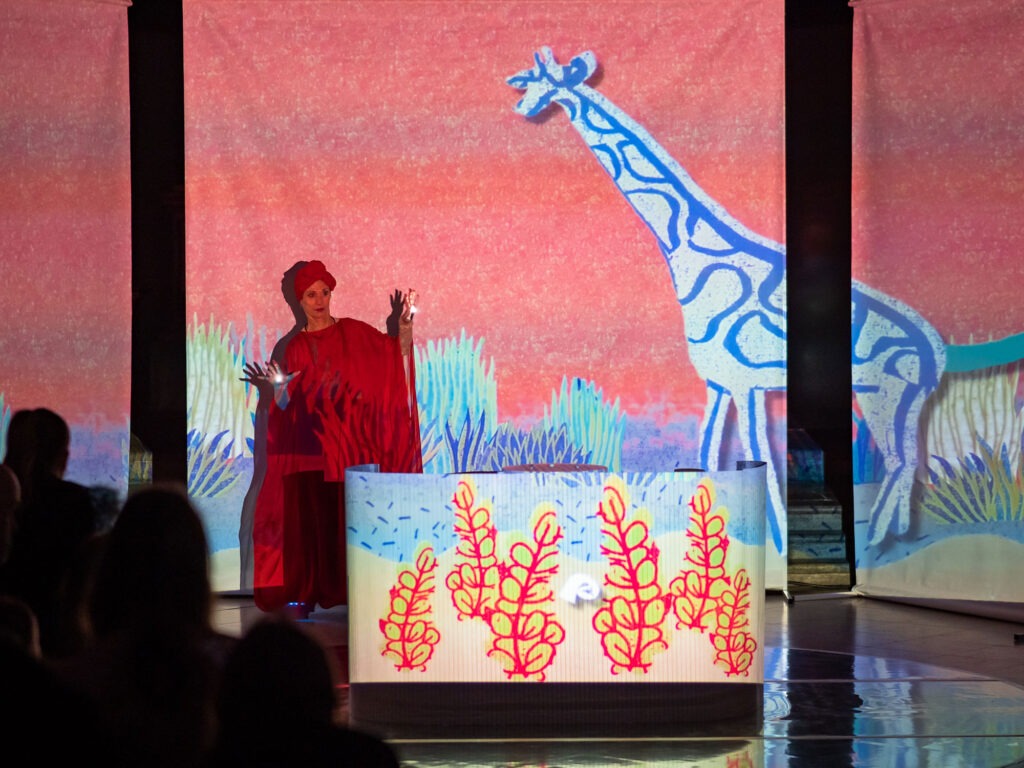 O kresbe, čo ožila, foto z divadielka. Žena v červenom, kresby a veľká nakreslená žirafa