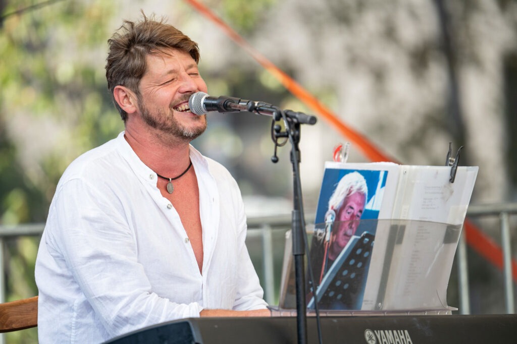 Spomienka na Deža 2024, na fotografii je spievajúci muž za  klavírom